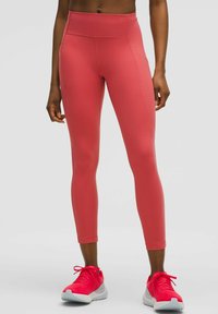 Leggings rosas de talle alto con una textura suave, costuras laterales y detalles sutiles. Combinados con zapatillas deportivas rosa brillante.