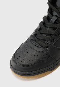 Zwarte synthetische leren sneaker met geperforeerde neus, zwarte veters en een gumrubber zool. Heeft een ronde vorm en versterkte stiksels.