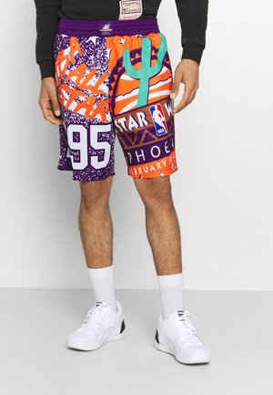 Mężczyzna noszący kolorowe spodenki do koszykówki NBA All-Star Phoenix 1995 oraz białe buty sportowe Puma na białym tle.