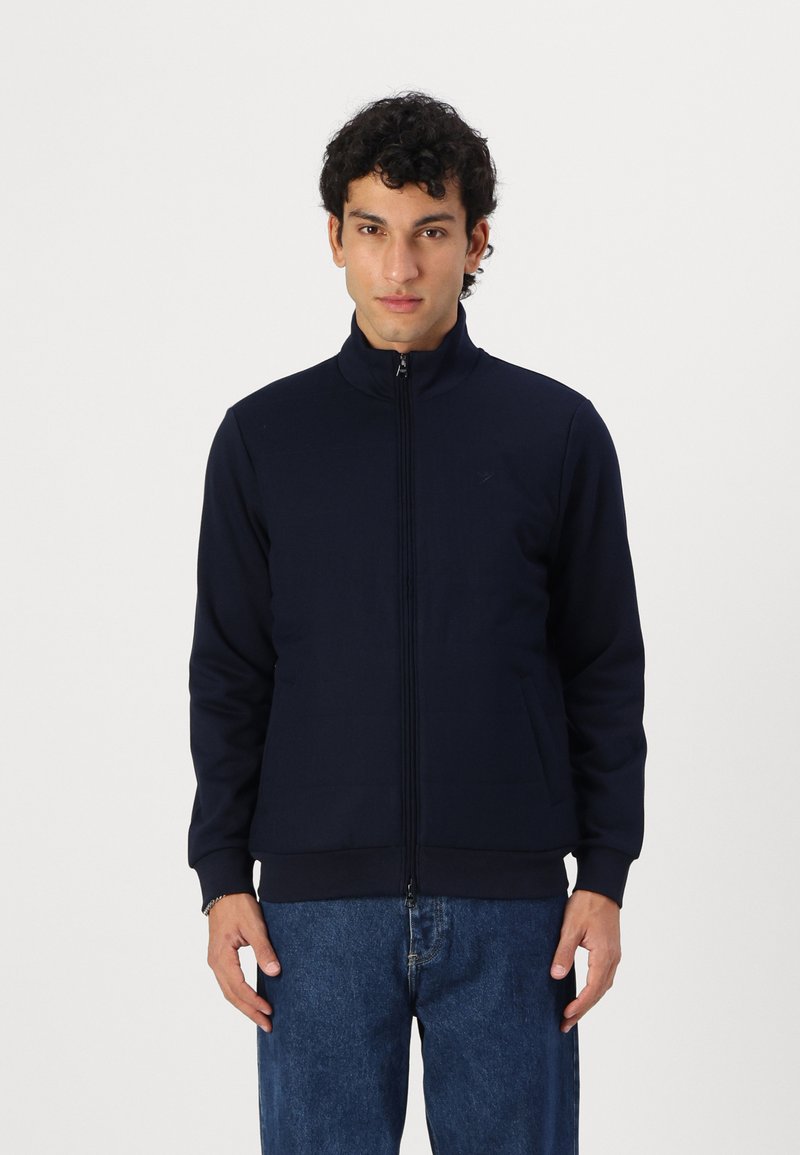 Laav navy zip-up takki korkealla kauluksella, ribbireunuksilla ja kahdella sivutaskulla. Tasainen rakenne ja vartalonmyötäinen muotoilu. Klassinen urheilutyylinen.