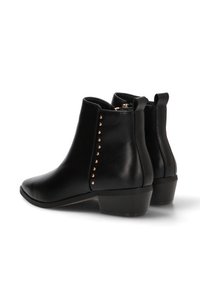 Botas de cuero negras hasta el tobillo con punta redondeada, tacón pequeño y tachuelas doradas decorativas a lo largo del lado exterior. Textura suave y diseño minimalista.