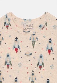 Light-colored shirt featuring a pattern of rockets, stars, and planets, with the brand label "HUST and CLAIRE" visible near the neckline.