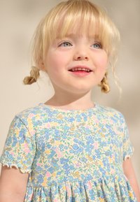 Lätt texturerad bomullsklänning med ett blommönster i blått, gult och rosa, med korta ärmar och vågiga kanter.