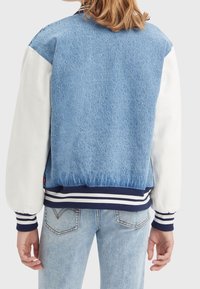 Džínová bunda s bílými rukávy, žebrovanými námořnickými a bílými manžetami a texturovaným modrým tělem. Neformální design s uvolněným střihem.