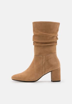 Tan suède laarzen met mid-kuit hoogte, slouchy design, blokhak en afgeronde neus, zijaanzicht op effen achtergrond.