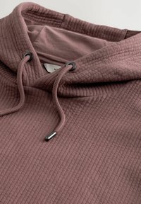 Sudadera con capucha en rosa empolvado, con textura acanalada, detalles en negro y cordones ajustables para un mejor ajuste.