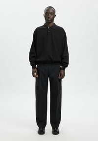 Czarna długo rękawowa koszulka polo z trzema guzikami, zestawiona z luźnymi czarnymi spodniami i czarnymi butami. Prosty design, gładka tkanina i luźny krój.