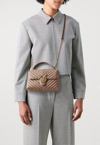 Gequiltete beige Lederhandtasche mit einem goldfarbenen Metallverschluss und Kettenriemen, die eine strukturierte Form und einen oberen Griff aufweist.