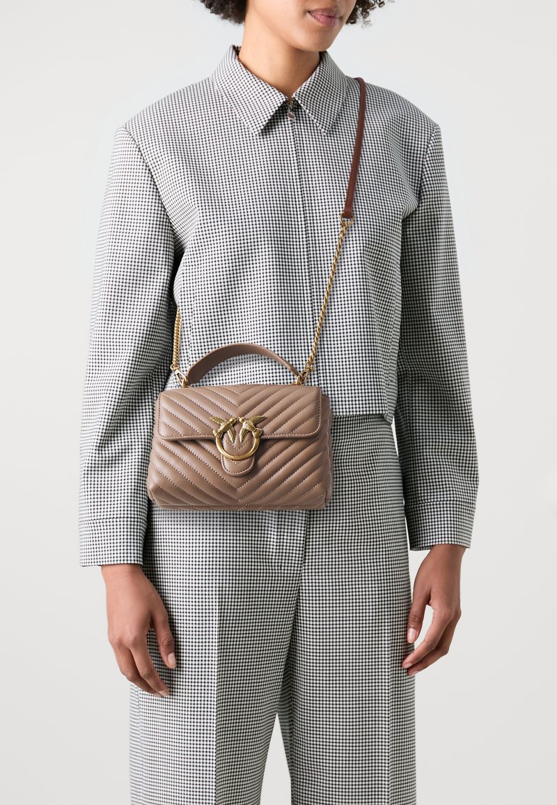 Gequiltete beige Lederhandtasche mit einem goldfarbenen Metallverschluss und Kettenriemen, die eine strukturierte Form und einen oberen Griff aufweist.