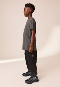 T-shirt gris en coton, coupe ample, associée à un pantalon cargo noir avec poches latérales. Baskets noires et grises avec surfaces texturées.
