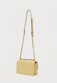 Κίτρινη τσάντα ώμου από καπιτονέ δέρμα με μοτίβο ζιγκ-ζαγκ, χρυσή αλυσίδα και ρυθμιζόμενο λουράκι ώμου. Περιλαμβάνει μεταλλικές διακοσμητικές λεπτομέρειες.