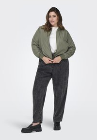 Olivovo zelená bomber bunda, biela tričko pod ňou, čierne strečové džínsy s kyselinovým umývaním a čierne platformové poltopánky.