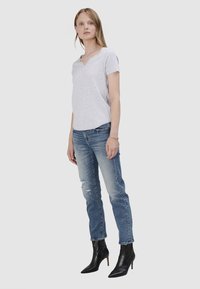 Jasnoszary, krótko rękawowy t-shirt z dekoltem w serek w połączeniu z przetartymi niebieskimi dżinsami i czarnymi, szpiczastymi botkami za kostkę, z dobrze dopasowaną sylwetką.