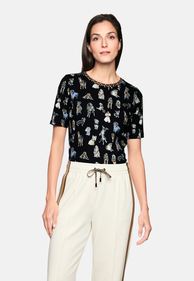 Black T-shirt featuring various dog illustrations, round neckline with leopard print accents. Paired with cream-colored joggers with side stripes.