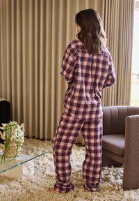Plaid loungewear set in purple and pink hues, featuring a relaxed fit, long sleeves, and matching pants, on a textured, soft rug.