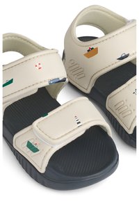 Μπεζ σανδάλι με μαύρη σόλα, με μοτίβα σκάφους και φάρου. Δύο ρυθμιζόμενοι ιμάντες με βέλκρο και υφασμένο πέλμα.