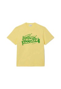 T- shirt in cotone giallo con logo di un coccodrillo verde e il testo "LACOSTE", con un semplice collo rotondo e maniche corte.