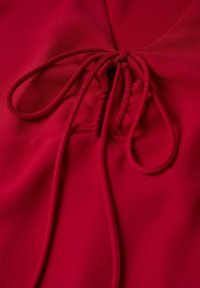 Tissu rouge avec un détail froncé noué en nœud à l’aide de fines cordelettes rouges au centre.