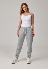 Graue Sweatpants mit elastischen Bündchen und Kordelzugbund, kombiniert mit einem weißen Tanktop. Das Model steht vor einem neutralen Hintergrund.