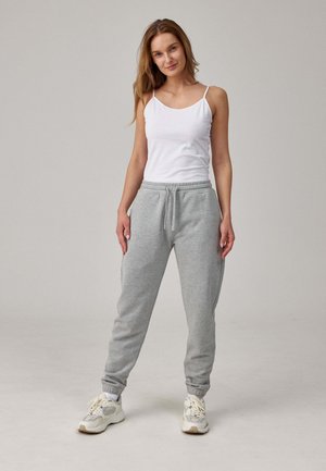 Pantaloni sportivi grigi con polsini elastici e vita con cordino, abbinati a una canotta bianca. Il modello è in piedi su uno sfondo neutro.