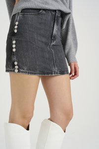 Zwarte spijkerrok met een sluiting met knopen aan de voorkant, zij-métallische knopen en een licht versleten structuur. Gecombineerd met knie-hoge witte laarzen.