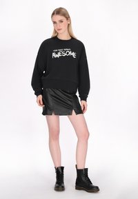 Fekete pulóver fehér felirattal, cropped fazonban, fekete bőr mini szoknyával, elöl hasított részekkel, és fekete fűzős harci csizmával párosítva.