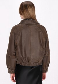 Giubbotto bomber in pelle marrone con una vestibilità rilassata, orlo a costine e maniche lunghe. Presenta un colletto classico e una finitura liscia e texture.
