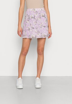 Saia floral roxa com flores brancas, design plissado, cintura elástica e tecido leve. Combinada com tênis brancos.