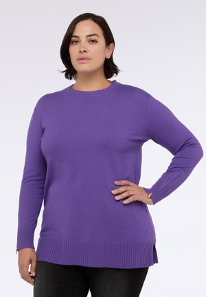 Suéter largo de manga larga de color púrpura con dobladillo y puños acanalados, que presenta detalles con cremallera en las muñecas. Fabricado con una tela suave y lisa.