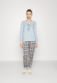 Lichtblauw langesleeve top met bloemenprint en de tekst "WILDFLOWERS", gecombineerd met beige en blauwe geruite broek. Zachte witte slippers.