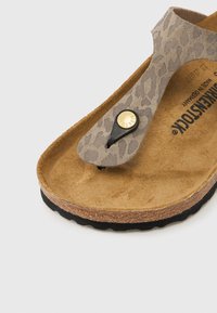 Ταμπά σανδάλι thong με επάνω μέρος σε σχέδιο λεοπάρδαλης, πάτο από φελλό και μαύρη καουτσούκ σόλα. Διαθέτει στρογγυλή χρυσή λεπτομέρεια κοντά στο σημείο του δακτύλου.