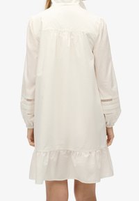 Abito bianco a maniche lunghe con fondo arricciato, pieghe frontali e dettagli cut-out sulle maniche. Tessuto morbido con una vestibilità comoda.