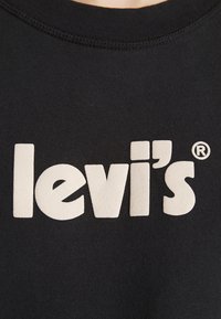 Sweatshirt noir avec un logo "levi's" en crème bien visible, en police épaisse et en majuscules. Le tissu a une texture lisse et un col côtelé.