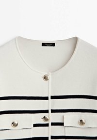 Vit cardigan med marinblå horisontella ränder. Funktioner med silverknappar och rund hals. Mjuk textur, detaljerad sömnad synlig.