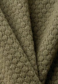 Gros plan sur un tissu tricoté vert olive texturé, avec une apparence douce et légèrement duveteuse et un motif de points tissés visible.