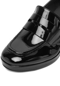 Črni lakasti loafer iz usnja z gladko površino, ki ima sprednji trak in šivane detajle ob robovih. Zaobljena zasnova prstnega dela.