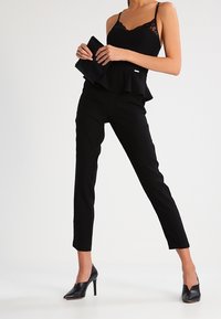 Camiseta sin mangas con encaje negro y dobladillo peplum, combinada con pantalones negro ajustados y elegantes tacones negros de punta.