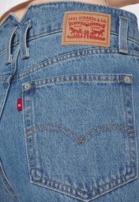 Modré džíny z denimu s koženou nášivkou označenou Levi Strauss & Co. Prošívání na kapsách, obsahující malý červený štítek a nýty.