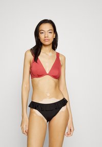 Top de bikini triangular vermelho com alças ajustáveis, combinado com um fundo de bikini preto com babados. Tecido suave com um acabamento mate.