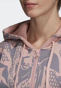 Mikina s kapucí v jemné růžové a šedé barvě s grafickým vzorem. Obsahuje přední zip a stahovací šňůrky na kapuci. Směs bavlny.