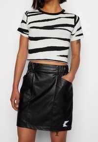 Stickad crop top med svart och vit zebra rand, tillsammans med en svart konstläderkjol med sidofickor och dragsko i midjan.