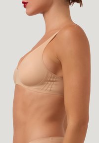 Beige formar bh med en slät textur, tunna justerbara axelband och subtila sidodetaljer. Snygg design med en mjuk finish.