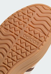 Adidasova potplat u svijetlo narančastoj boji s teksturiranim uzorkom za prianjanje, središnjom prugom i ugraviranim imenom branda za bolju trakciju i izdržljivost.