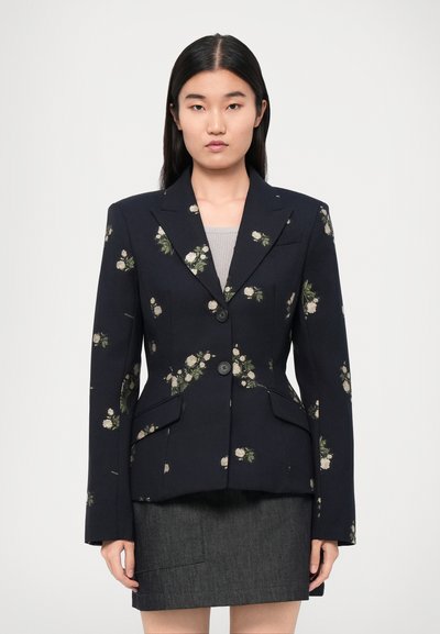 Marineblazer mit floralem Muster, tailliertem Design, zwei Knöpfen und zwei frontalen Taschen. Kombiniert mit einem dunkelgrauen Rock.