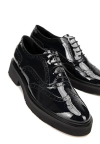 Černé lakované kožené boty s brogue detaily, šněrovací design, zvýšená podrážka a texturované akcenty. Hladký povrch s lesklým vzhledem.