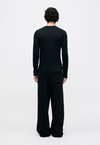 Black long-sleeve shirt with a round neckline, fitted design, and smooth texture. Paired with loose-fitting black pants featuring a back pocket.