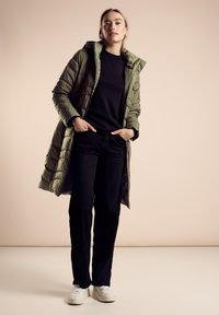 Zielona kurtka puchowa z kapturem, czarna koszulka z długim rękawem, czarne spodnie i białe trampki. Kurtka ma przeszycia oraz zamek.