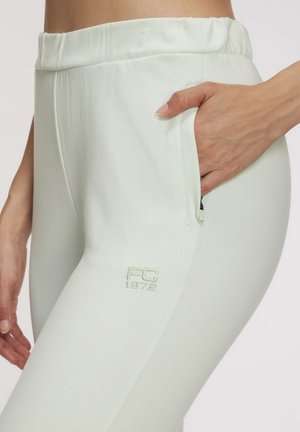 Pantalones de chándal verde claro con una cinturilla elástica, que cuentan con bolsillos laterales y un sutil logotipo bordado "FC 1972" en el muslo.