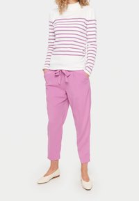 Top blanco de manga larga con rayas rosas, combinado con pantalones rosa de cintura alta que tienen un lazo en la cintura y un corte relajado.