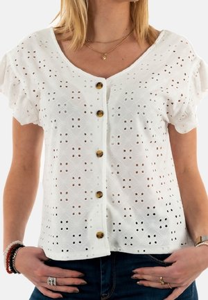Blouse blanche à manches courtes volantées, ornée de motifs brodés et de découpes, agrémentée de boutons marron sur le devant.